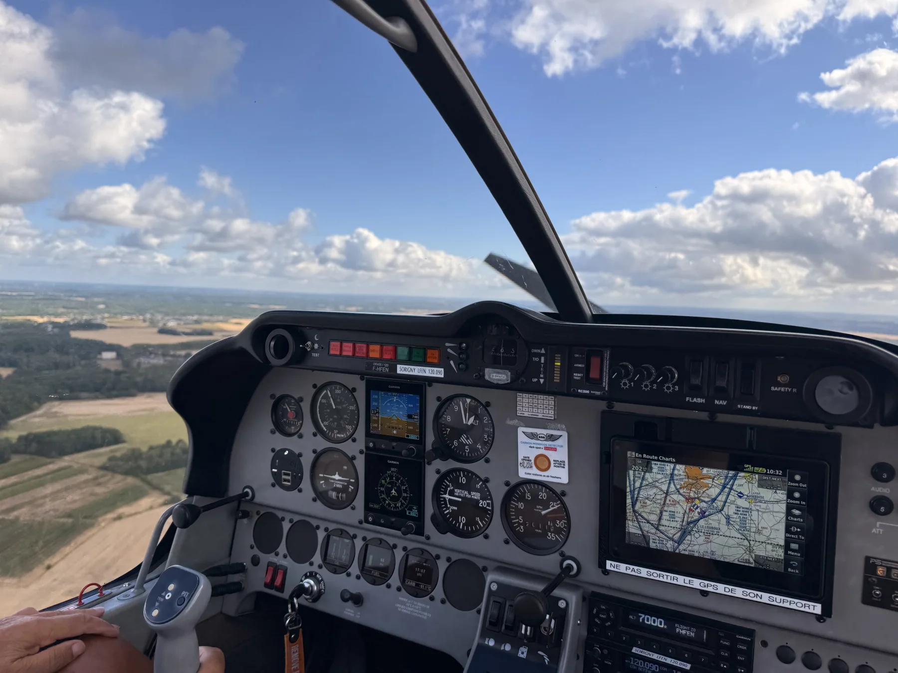 Tableau de bord d’un Robin DR401 en vol devant un ciel bleu nuageux