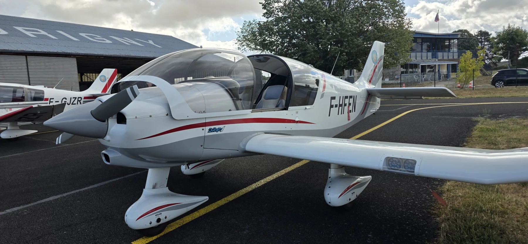 Robin DR401 F-HFEN blanc et rouge stationné devant un hangar